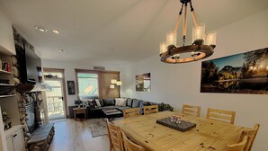 A spacious living area with a wooden dining table, a sofa, and a fireplace. - Modern Mountain Retreat - Walk to Village + HotTub (Beaverdell)
