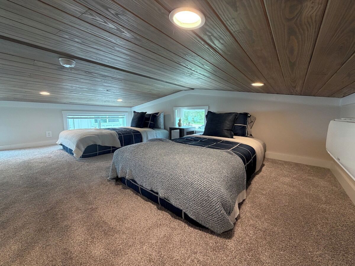 A bedroom with a sloped ceiling, a large bed, a smaller bed, and a window.