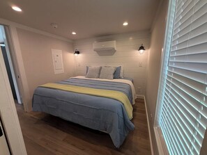 Un dormitorio con cama, lámparas de noche, aire acondicionado y una ventana con persianas.