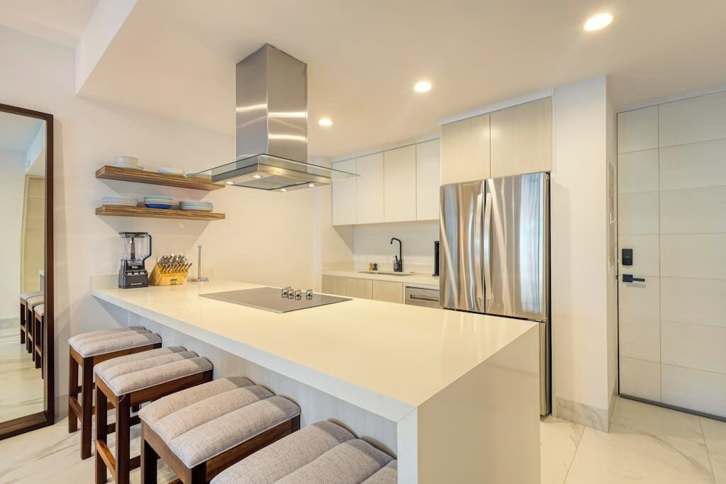 A modern kitchen with a central island, stainless steel appliances, and wooden bar stools.