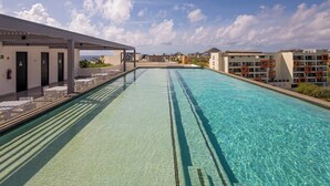 A swimming pool with clear water, a covered seating area, and buildings in the background. - Family-friendly Oasis With Pool and Steps From Medano Beach (Cabo San Lucas)