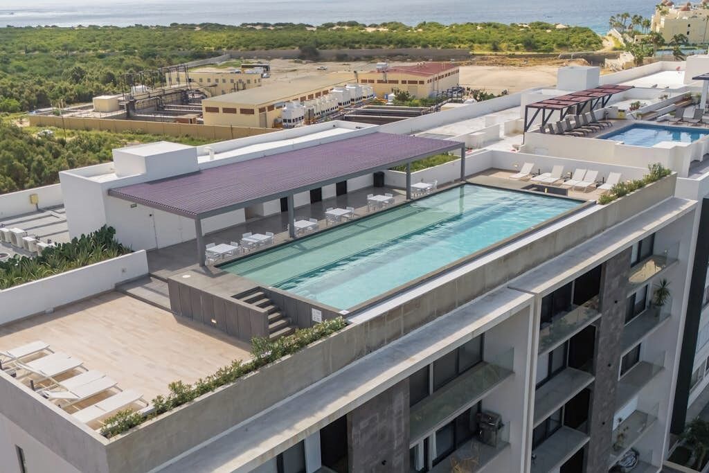 A rooftop pool with lounge chairs, a covered area, and a view of the sea and buildings.