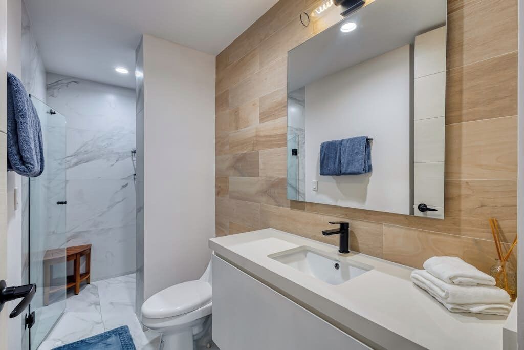Un baño moderno con cabina de ducha de vidrio, inodoro blanco, tocador con lavamanos y espejo.