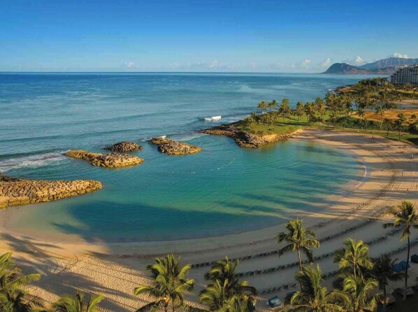 Ein Küstenort mit klarem türkisblauem Wasser, einem Sandstrand und Palmen.