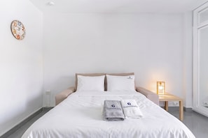 Une chambre d’hôtel comprenant un lit, des oreillers, une horloge, une table de chevet, une lampe et des serviettes portant un logo.