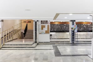 Un hall d’hôtel avec un escalier en marbre, un comptoir d’accueil et un présentoir à chaussures.