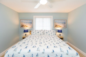 A bedroom with a bed, two nightstands, a ceiling fan, a window with blinds, and two wall-mounted lamps. - Bay Breeze Retreat: Lakefront Condo with Pool (Put-in-Bay)