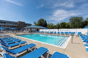 Une piscine entourée de chaises longues bleues et de parasols, le tout bordé par un bâtiment à la façade en pierre et au toit bleu.