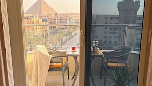 Une chambre avec vue sur une pyramide et une tour, un balcon avec des chaises et une table, et une plante en pot.