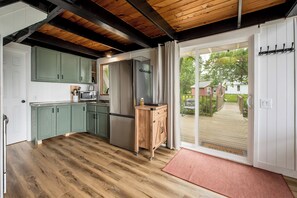 A kitchen with wooden flooring, green cabinets, a stainless steel refrigerator, and a wooden sideboard.