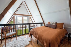 A bedroom with a bed, a chair, a fur rug, and a balcony with a view of the outdoors.