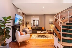 A modern living room with a sofa, armchairs, a coffee table, and a TV. There's a staircase with wooden railings and a view of the outside. - House in Soho Heated Pool, BBQ Grill & Playroom (Buenos Aires)