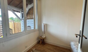 Une piĂšce dotĂ©e dâune grande fenĂȘtre, dâun ventilateur sur pied, dâun tabouret en bois et dâune porte avec une poignĂ©e en mĂ©tal.