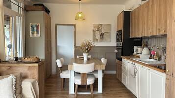 Een moderne keuken met houten kastjes, een eettafel met stoelen, een hanglamp en een schilderij aan de muur.