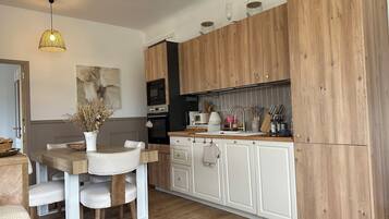 Een moderne keuken met houten kastjes, een eettafel met stoelen, een hanglamp en een vaas met gedroogde bloemen.