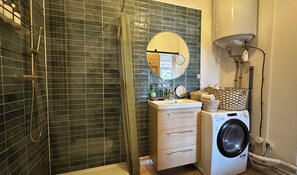 Une salle de bain avec une douche, un lavabo avec un miroir, un lave-linge et un porte-serviettes.