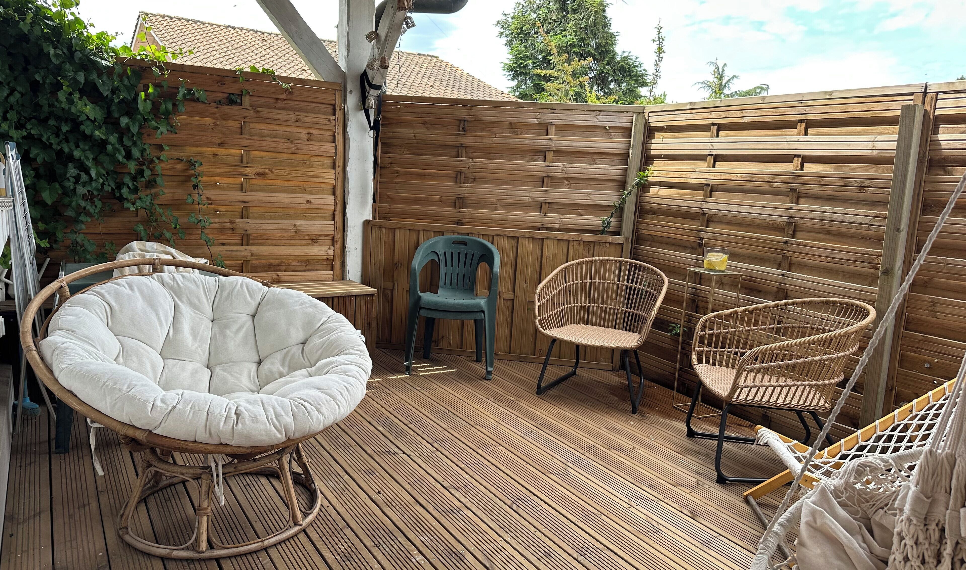 Een houten terras met rieten meubels, waaronder een stoel en een bijzettafeltje met een drankje.