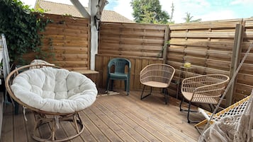 Een houten terras met rieten meubels, waaronder een stoel en een bijzettafeltje met een drankje.