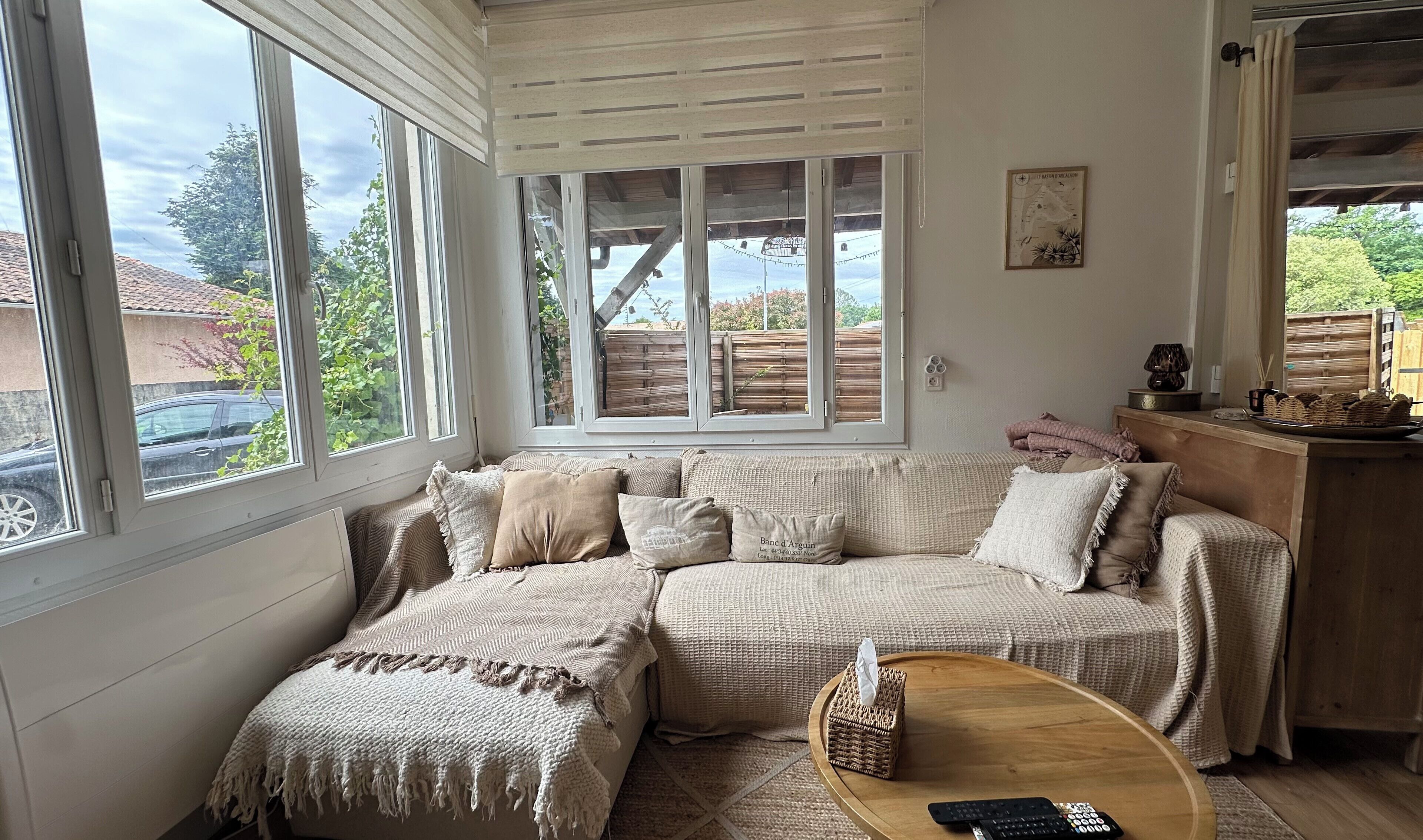 Une pièce chaleureuse avec une grande fenêtre, un banc en bois, un panier en osier et une télécommande posée sur une table en bois.. Appartement avec grande terrasse à Biganos
