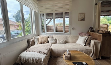 Une pièce chaleureuse avec une grande fenêtre, un banc en bois, un panier en osier et une télécommande posée sur une table en bois.. Appartement avec grande terrasse à Biganos