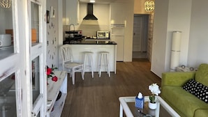 A modern kitchen with white cabinets, a black range hood, and a microwave. There are two white bar stools and a green sofa in the living area. - Apartment 'Chris' with Shared Pool, Wi-Fi, and Air Conditioning (Benalmádena)