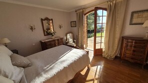 Ein Schlafzimmer mit Bett, Kommode, Spiegel und Blick durch eine offene Tür.