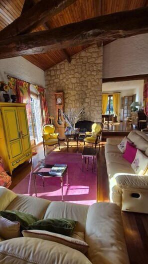 Ein gemütliches Wohnzimmer mit Steinwand, Holzbalken, gelben Sesseln, einem weißen Sofa und einem Kamin.