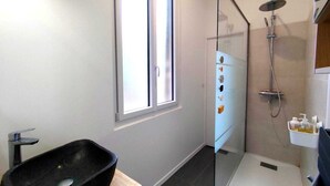 Een moderne badkamer met een douchecabine van glas, een zwart wastafelmeubel en een raam voor natuurlijk licht.