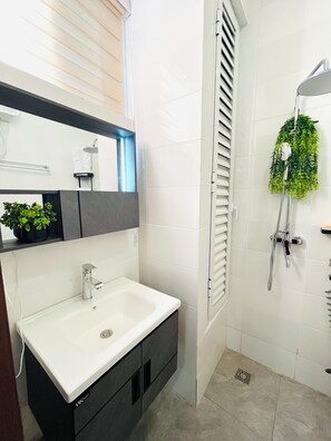 A bathroom with a white sink, a mirror, a shower with a green plant, and a toilet.