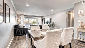Un coin repas avec une table en bois, des chaises à revêtement blanc et un canapé noir.