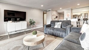 Un salon moderne avec un canapé gris, une table basse ronde et un téléviseur à écran plat fixé au mur.