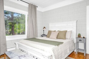 Ein Schlafzimmer mit großem Fenster, einem Bett mit Kopfteil, einem Nachttisch und einem Beistelltisch.