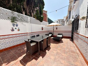 Eine Terrasse im Freien mit Tisch und Stühlen, einem dekorativen Zaun und einer gefliesten Wand mit einem gemusterten Fries.