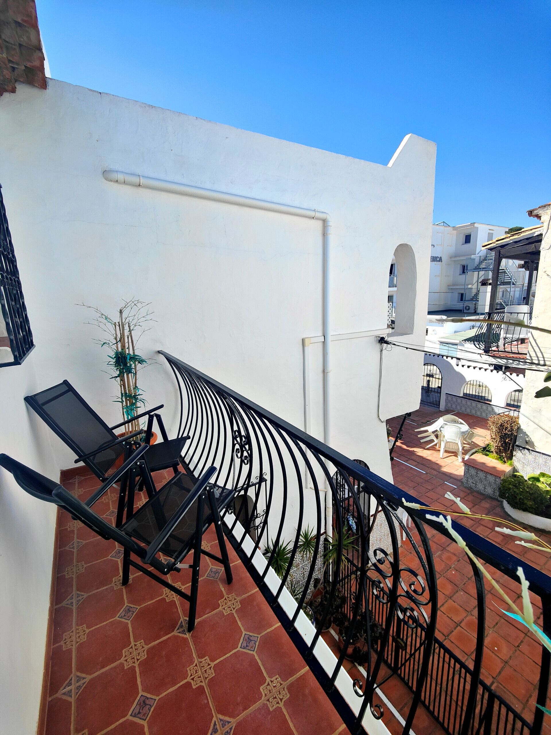 Balcón con caminadora, mobiliario exterior y vista de edificios cercanos.