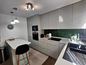 Eine moderne Küche mit weißer Arbeitsplatte, einem schwarzen Stuhl, einer Mikrowelle und einer grünen Spritzschutzwand.