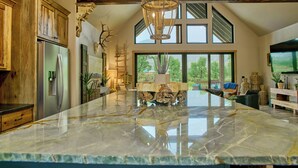 A spacious kitchen with a large marble island, wooden cabinets, and a modern chandelier. - RiverBend Rio (South Fork)