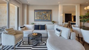 A modern living room with a sectional sofa, a coffee table, and a dining area with chairs. - Elegant Resort Condo With Heated Pool, Pickleball, gym & Garden Views (Cabo San Lucas)