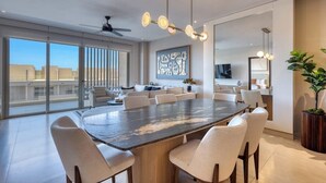 A spacious dining area with a large table, multiple chairs, a ceiling fan, and a large window offering a city view. - Elegant Resort Condo With Heated Pool, Pickleball, gym & Garden Views (Cabo San Lucas)