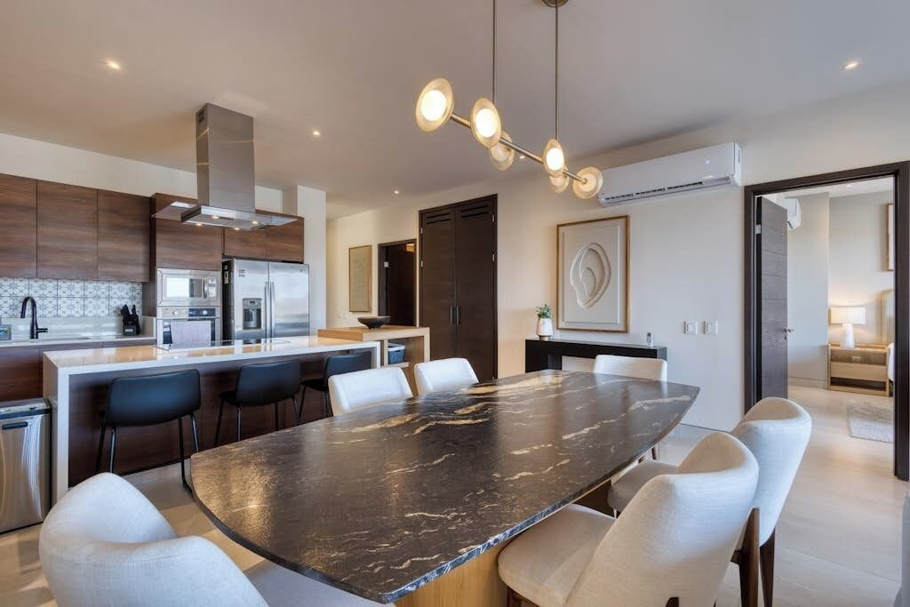 A modern kitchen with a central island, stainless steel appliances, and a dining area with a marble table.