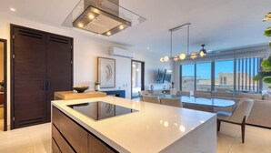 A modern kitchen with a large island, dark wooden cabinets, and a dining area with a glass table and chairs. - Elegant Resort Condo With Heated Pool, Pickleball, gym & Garden Views (Cabo San Lucas)