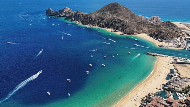 An aerial view of a coastal area with boats, a beach, and buildings. - Elegant Resort Condo With Heated Pool, Pickleball, gym & Garden Views (Cabo San Lucas)