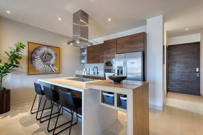 Una cocina moderna con una isla central, taburetes de bar, un refrigerador de acero inoxidable y un cuadro decorativo grande.