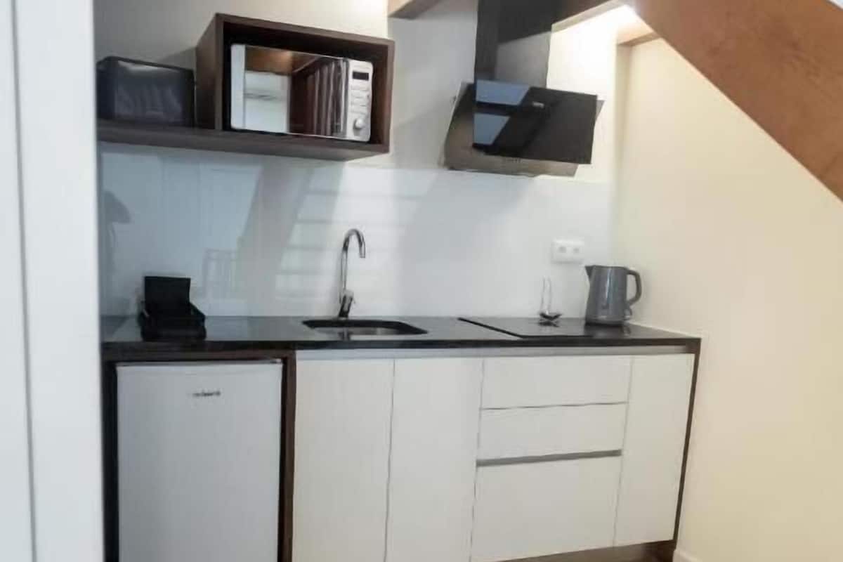Una cocina compacta con armarios blancos, microondas integrado y un lavamanos.
