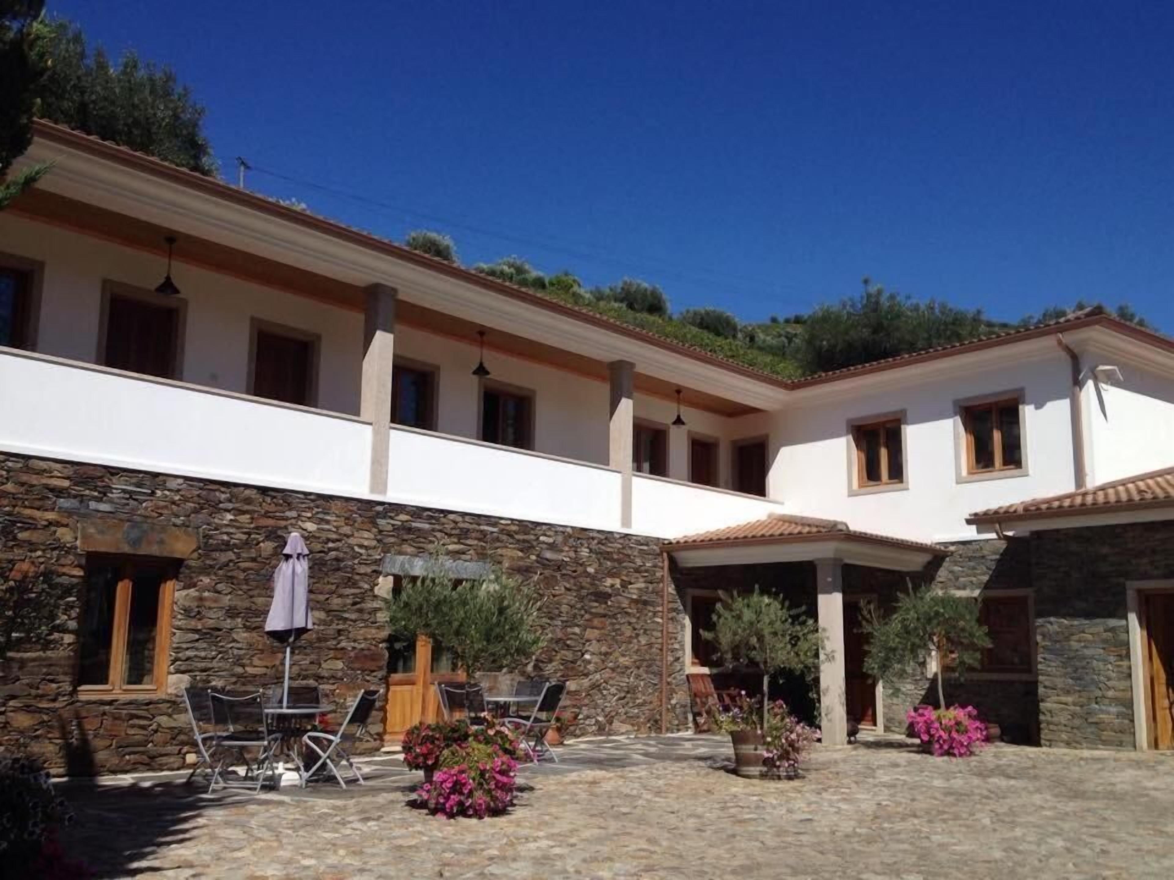 Un bâtiment à la façade en pierre, un patio couvert avec des sièges en plein air, et un ciel d’un bleu éclatant.