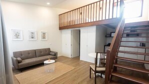A living room with a sofa, a coffee table, a chair, a staircase, and a door leading to a kitchen.
