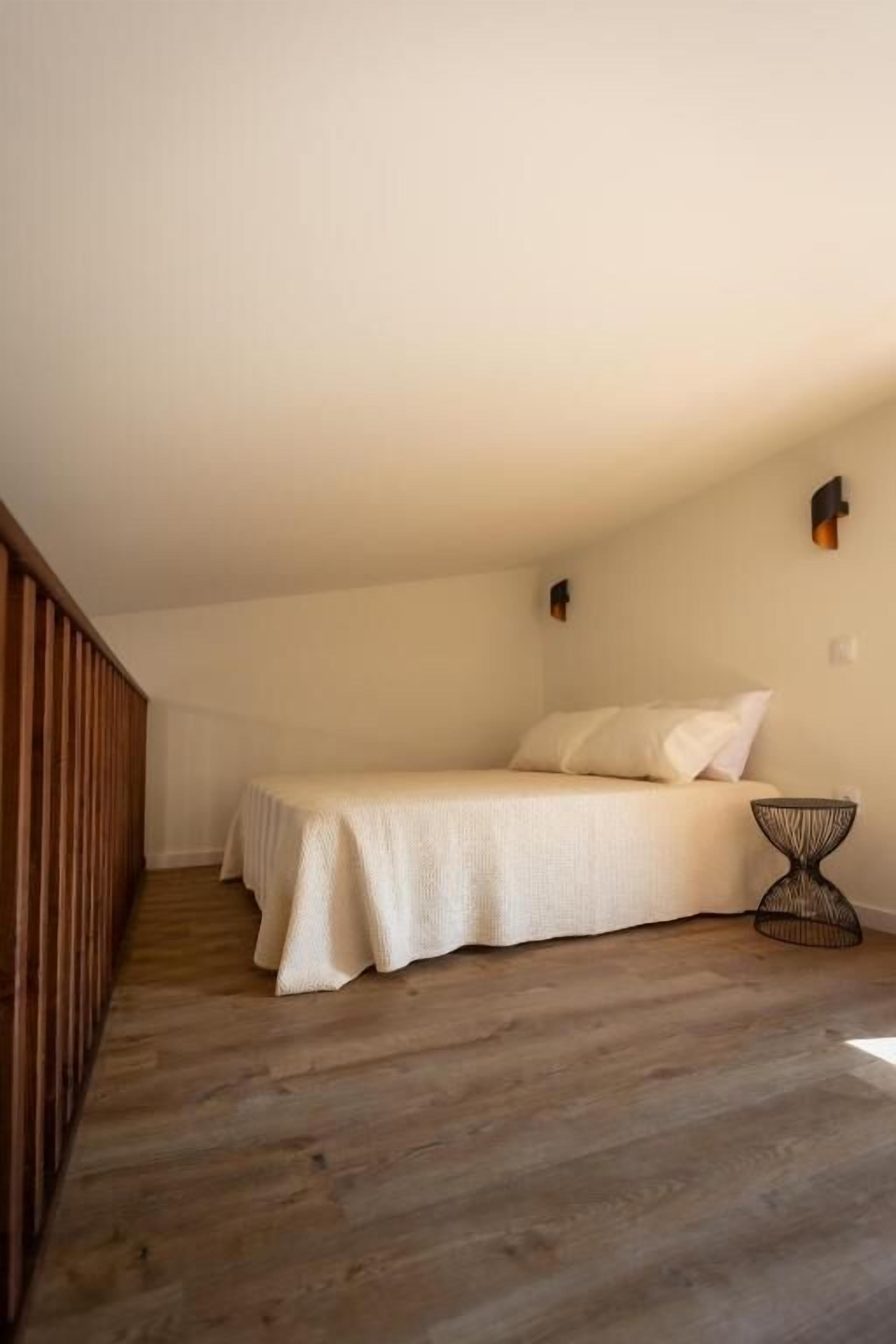 A bedroom with a bed, a small table, and a wooden floor.