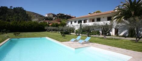 A swimming pool with lounge chairs, a grassy area, and a building with a red-tiled roof.