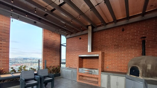 Een terras buiten, met een bakstenen muur, een bakoven en een zithoek met stoelen en een tafel.