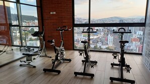 Een sportschool met fitnessapparatuur en grote ramen met uitzicht op de stad.