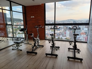 Ein Fitnessstudio mit Trainingsgeräten und großen Fenstern, die einen Blick auf die Stadt ermöglichen.